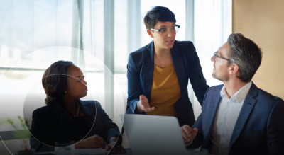 A person stands, gesturing while two seated individuals listen attentively