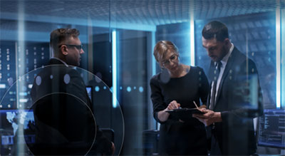 Three people in business attire review information in a data center