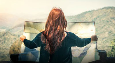 Person standing outdoors and holding a large map while looking out toward distant mountains and a hazy landscape