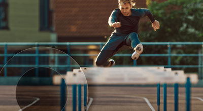 A person in mid-air performing a jump over a metal hurdle on a gymnastic track