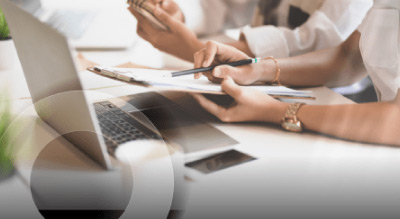 A group of people working together at a desk with a laptop and papers