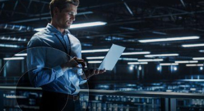 A man holding a laptop in a server room illuminated by blue lighting