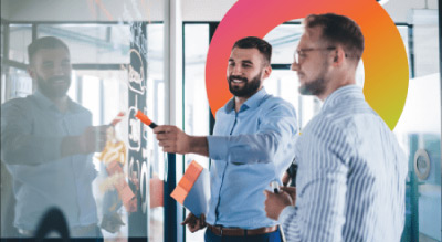 Individuals in a meeting, standing in front of a whiteboard adorned with post-it notes in a modern office