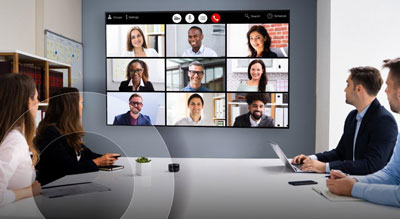 Two people in a modern office attending a virtual meeting with multiple participants displayed on a large screen