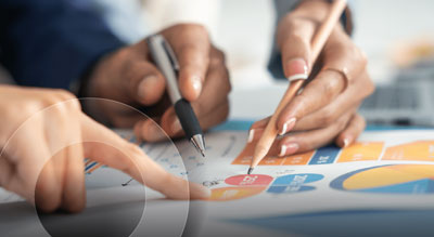 Three hands point at a circular graph chart using pencils