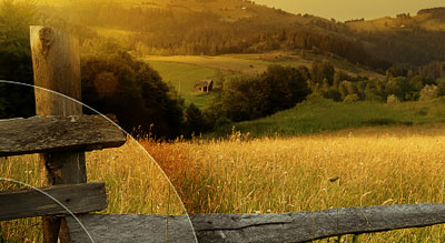 A wooden fence in a field with a view of a hill and trees with a warm, golden tone