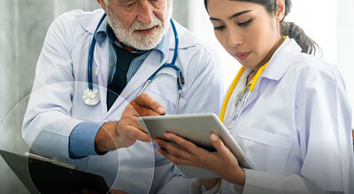 Two healthcare professionals in white coats review information on a tablet.