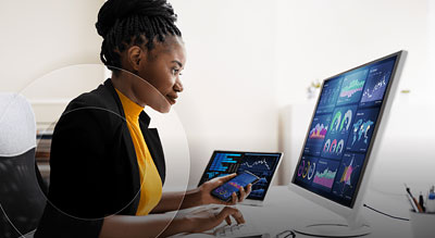 A person sitting at a desk with a computer monitor and a tablet, analyzing data