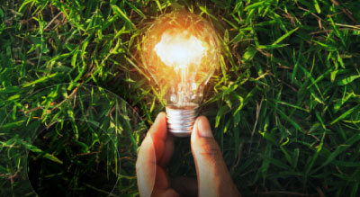 A hand holds a glowing light bulb above green grass
