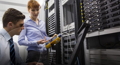 Two professionals examining a server rack with a diagnostic tool in a well-organized data center