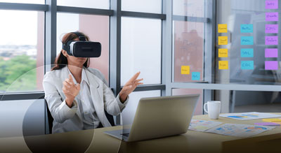 A person is seated at a desk, wearing a virtual reality headset and gesturing with their hands