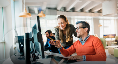 Two employees pointing at a computer and smiling in an office setting