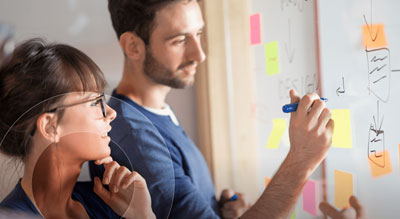 Two people collaborating and writing on a whiteboard covered with colorful sticky notes