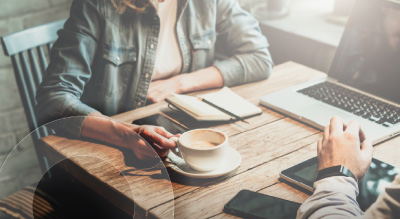Two people seated at a table, working on a laptop with coffee cups beside them