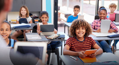 Smiling children in classroom using tablet devices