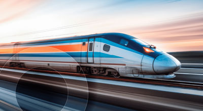 A sleek blue and white high-speed train races along the tracks against a backdrop of a sunset