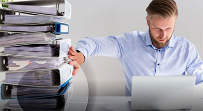 A professional man multitasking with a laptop and files on his desk