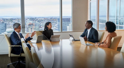 Four business professionals engaged in discussion around a conference table while using Microsoft Surface devices
