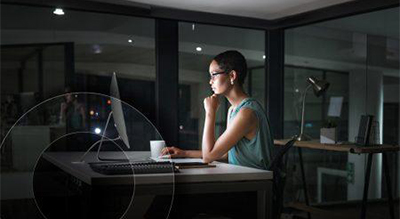 Person sitting at a desk in a dimly lit room at night, working on a desktop computer