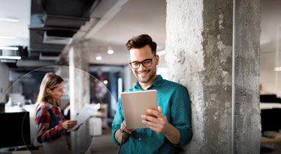 Smiling individual uses a tablet in a busy office