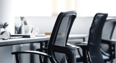 A bright, modern office space with empty ergonomic chairs at sleek desks. Items like a mug, notebook, and headphones suggest a clean, professional environment.