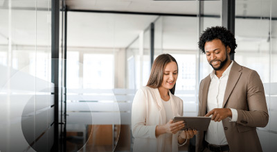 Two individuals standing in a modern office environment, holding and looking at a tablet
