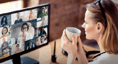 Person engaging in a video conference with multiple participants on their computer screen, holding a mug