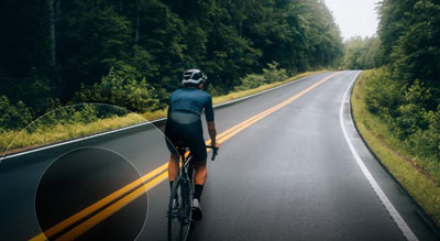 A cyclist is riding on a wet road amidst lush greenery