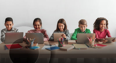 A group of children working on laptops at a table surrounded by stationery and craft items