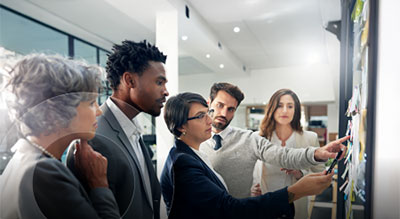 Group of colleagues gathered around a wall display, reviewing notes and discussing project ideas in a modern office setting