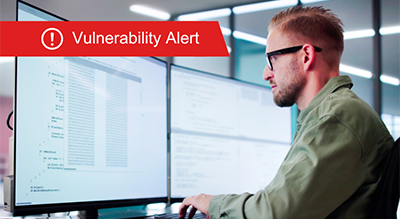 A man wearing glasses works on a computer displaying a vulnerability alert message on the screen