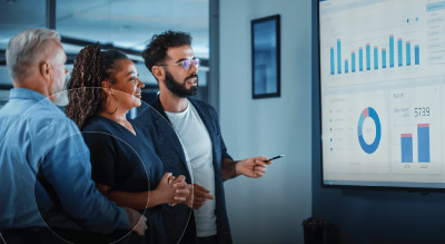 Three professionals analyze graphs on a screen during a business meeting in a modern office setting.