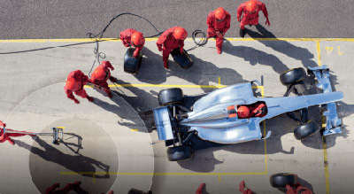 Overhead view of a Formula 1 pit stop. Crew members in red uniforms service a silver race car on a track.