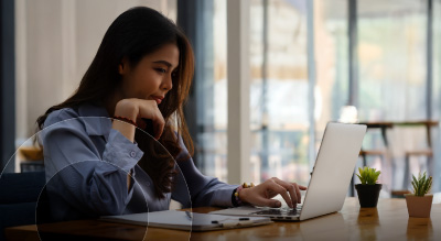A woman seated at a table, focused on her laptop
