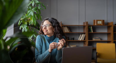 A person is sitting on a couch and using a laptop next to a window