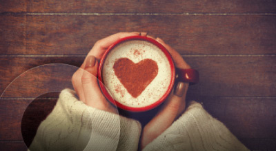 Hand holding a mug of coffee with a heart design in the foam