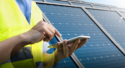 A close up of an employee near solar panels using a cell phone to send an sms message