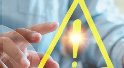 A person’s hand pointing at a yellow warning sign with an exclamation mark on a laptop screen