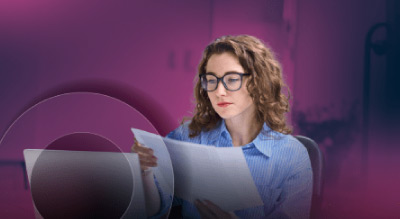 A person reading papers sits behind a laptop