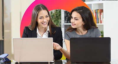 Two individuals sitting at a table and working on laptops