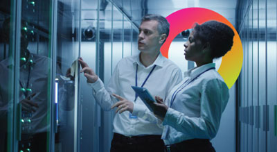 Two people inspecting a server rack in a data center while holding a tablet