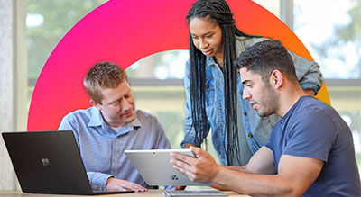 Three individuals collaborating on a task, two using laptops and one holding a tablet.