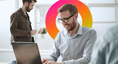 A man with glasses and a smile focused on his work while using a laptop.