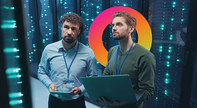 Two workers standing in a server room holding a laptop