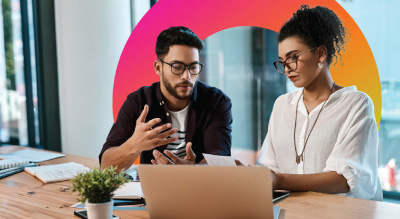 Two individuals seated at a table, collaborating over a laptop.