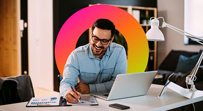 A person is working at a desk with a laptop and a phone, illuminated by a desk lamp