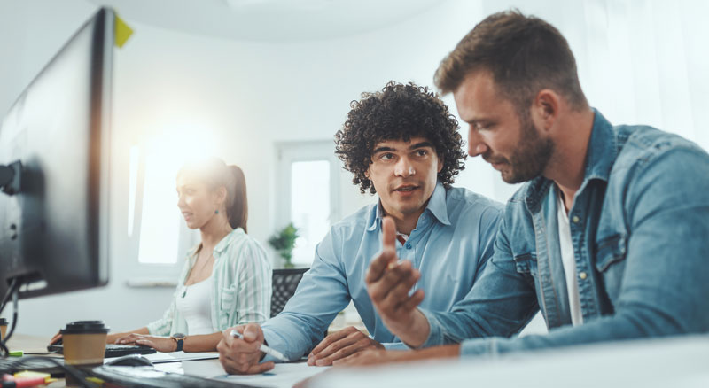 Two people are discussing work and collaborating at a desk with a computer