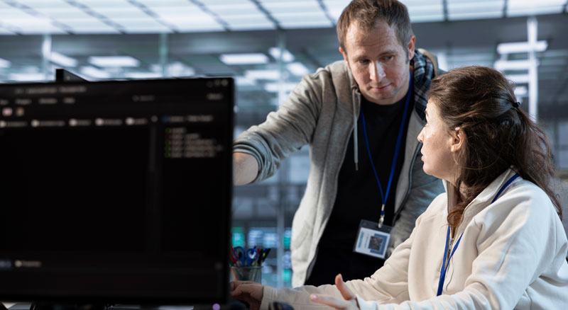 Two IT specialists having a conversation while sitting behind a monitor