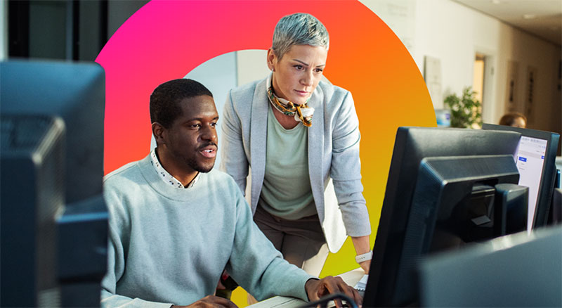 Two employees review information on desktop monitors