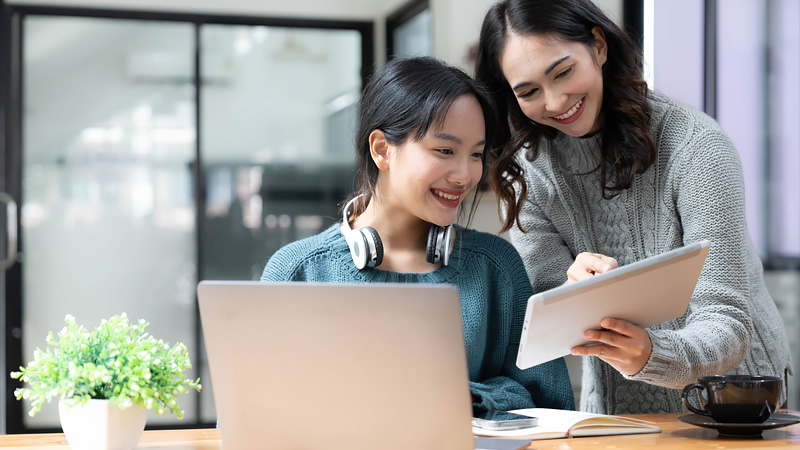 Woman using latops looks over at tablet another person is pointing towards